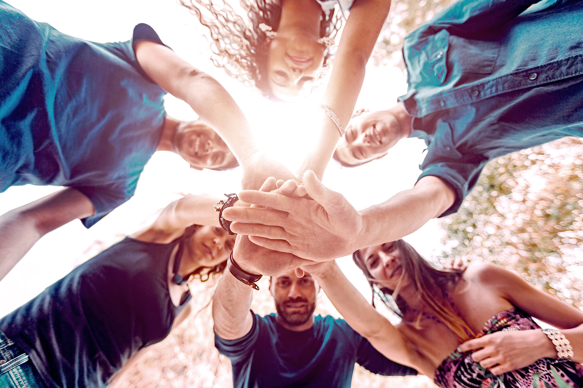 Multiracial group of friends with hands on stack and looking down at camera. They are six persons, three boys and three girls, on their early twenties. Teamwork and cooperation concepts.