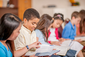 A multi-ethnic group of elementary age children are sitting together and are reading the Bible.