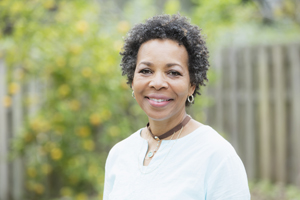 Portrait of a mature African-American woman in her 50s standing outdoors in the back yard by a fence. She is smiling at the camera.