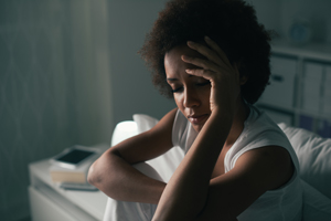 Sad depressed woman suffering from insomnia, she is sitting in bed and touching her forehead, sleep disorder and stress concept