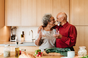 Happy man and woman looking at each other at kitchen island. Senior couple is holding alcoholic drink in kitchen. They are standing with arm around.