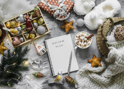 Christmas cozy home background. Christmas planning notepad, toys, hot chocolate, slippers, basket with knitted blanket on a gray background, top view