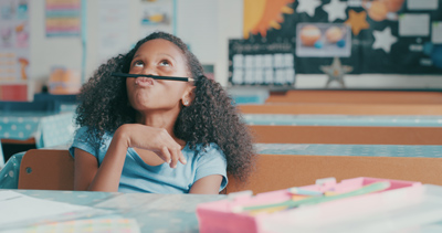 Shot of a young girl looking bored while fidgeting with a pencil at a school desk. Stimming ADHD. Fidgeting ADHD.